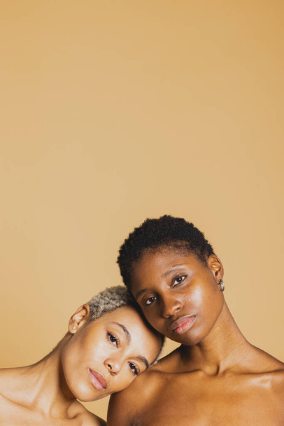 Portret van twee jonge Afro-Amerikaanse vrouwen op bruine achtergrond. close-up van twee jonge vrouwen met gesloten ogen. - Foto, afbeelding