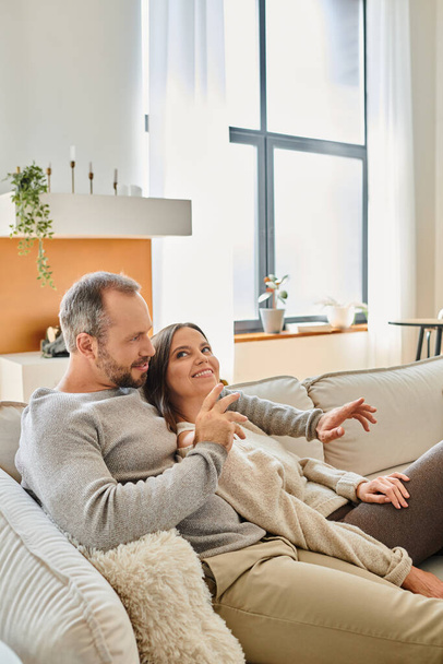 joyful child-free couple sitting on comfortable couch and talking in modern living room at home - Photo, Image