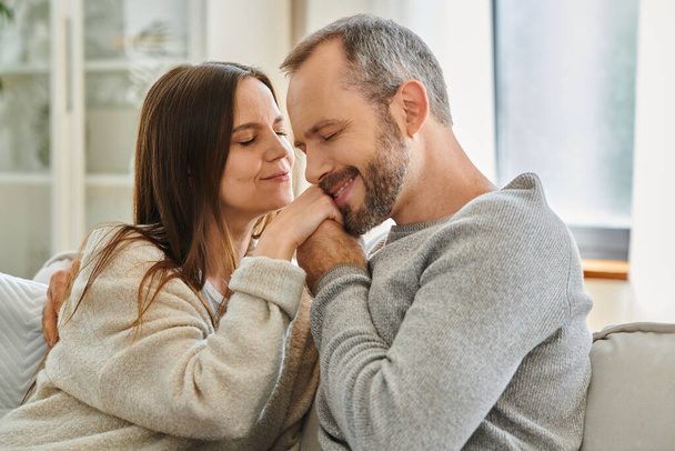 glücklicher Mann mit geschlossenen Augen, der die Hände seiner entzückten Frau im Wohnzimmer küsst, Liebe und Zärtlichkeit - Foto, Bild