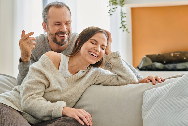 excited child-free couple laughing on couch in modern cozy living room, relaxation and fun at home - Photo, Image