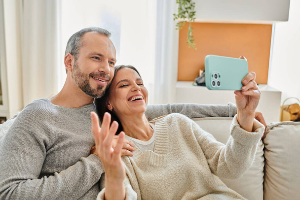 vrolijke vrouw het nemen van selfie op smartphone met echtgenoot in de woonkamer, vrije tijd van kind-vrij paar - Foto, afbeelding