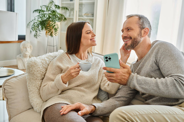 любляча дружина з чашкою кави торкається обличчя щасливого чоловіка на дивані у вітальні, бездітне життя - Фото, зображення