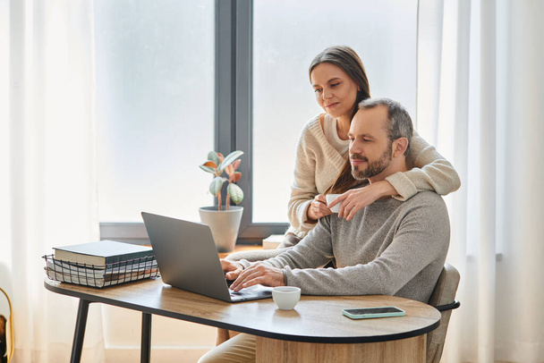 ondersteunende vrouw met koffiekopje knuffelen echtgenoot werken op laptop in huis kantoor, kind-vrij paar - Foto, afbeelding