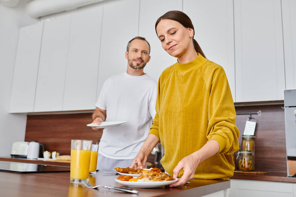 весела бездітна пара, що подає смачний сніданок на сучасній кухні разом, безтурботність і гармонію - Фото, зображення