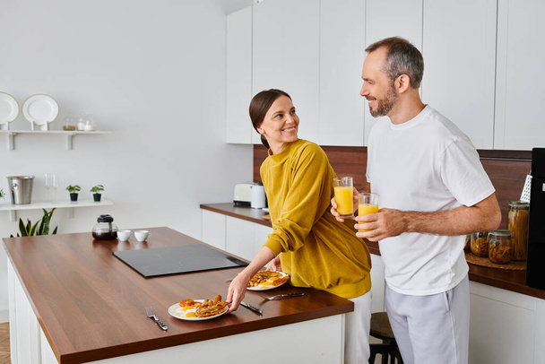 mujer alegre que sirve el desayuno cerca del marido con jugo de naranja en la cocina, estilo de vida libre de niños - Foto, imagen