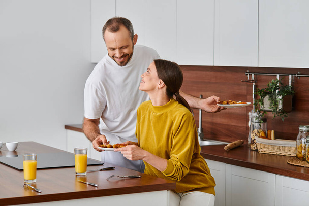 ευτυχισμένος άνθρωπος που σερβίρει νόστιμο σπιτικό πρωινό κοντά στη σύζυγο στην κουζίνα, το πρωί του ζευγαριού χωρίς παιδιά - Φωτογραφία, εικόνα
