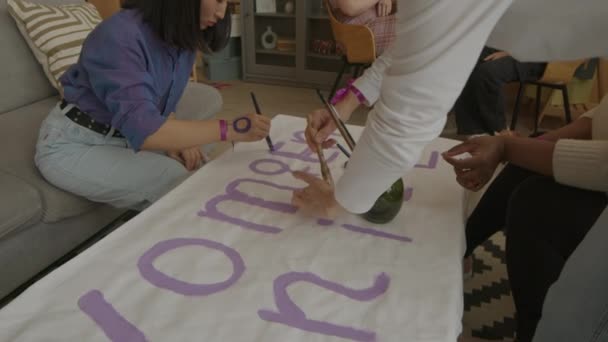Медленность многонациональной команды молодых независимых феминистских активистов, пишущих лозунг протеста на бумаге во время подготовки к демонстрационной встрече - Кадры, видео