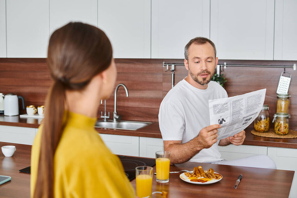 キッチンでおいしい朝食を楽しんでいる妻の近くの新聞を読んで驚いた男,子供なしのカップル - 写真・画像