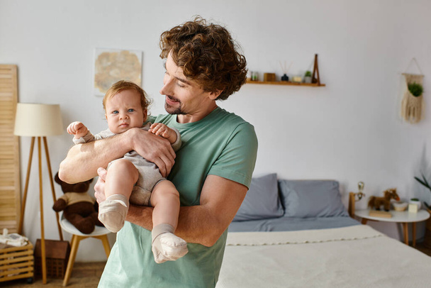 kręcone włosy i szczęśliwy ojciec trzyma swoje dziecko chłopiec w przytulnej sypialni w domu, ojcostwo - Zdjęcie, obraz