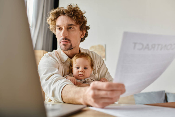 drukke alleenstaande vader houdt zuigeling zoon en contract in handen terwijl het werken vanuit huis, werk-leven evenwicht - Foto, afbeelding
