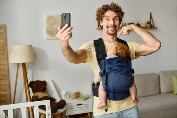 radosny ojciec robi selfie ze śpiącym dzieckiem w nosicielce, ojcostwie i nowoczesnej koncepcji rodzicielstwa - Zdjęcie, obraz