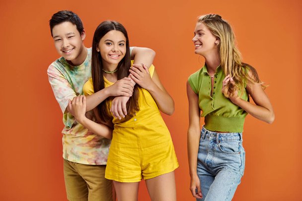 красивые веселые разнообразные подростки в повседневных нарядах улыбаются и обнимаются на оранжевом фоне - Фото, изображение