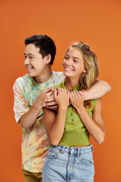 multiracial cheerful teenagers in vibrant attires hugging and looking away, friendship day - Photo, Image