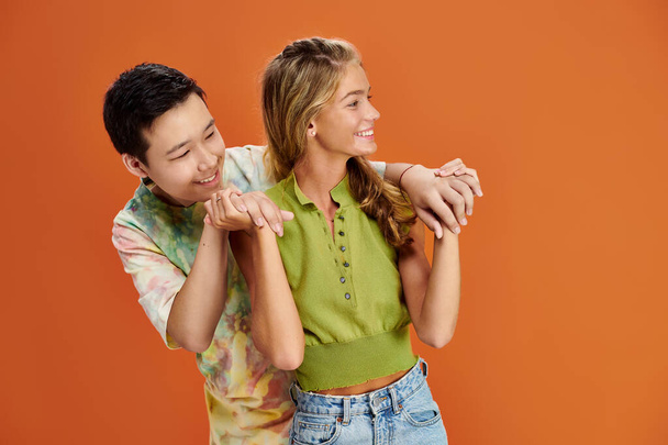 jolly multiracial friends in vivid clothes hugging and looking away on orange backdrop, friendship - Photo, Image