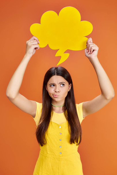 fokussiertes adoleszentes Mädchen in Alltagskleidung mit gelber Gedankenblase auf orangefarbenem Hintergrund - Foto, Bild