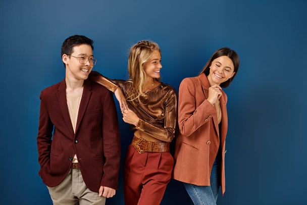 fröhlich stylische diverse Jugendliche in trendigen Anzügen lächeln glücklich auf blauem Hintergrund, Freundschaftstag - Foto, Bild