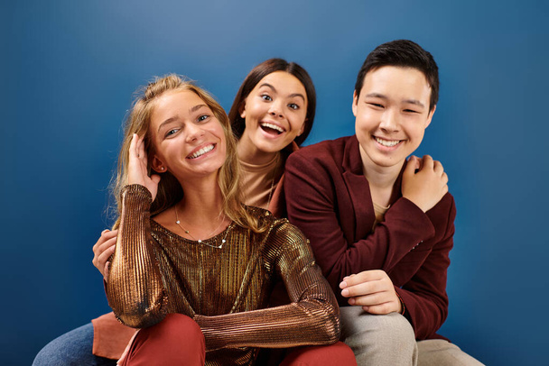 fröhliche multirassische Jugendliche in stylischen Outfits, die vor blauem Hintergrund in die Kamera lächeln, Freundschaftstag - Foto, Bild