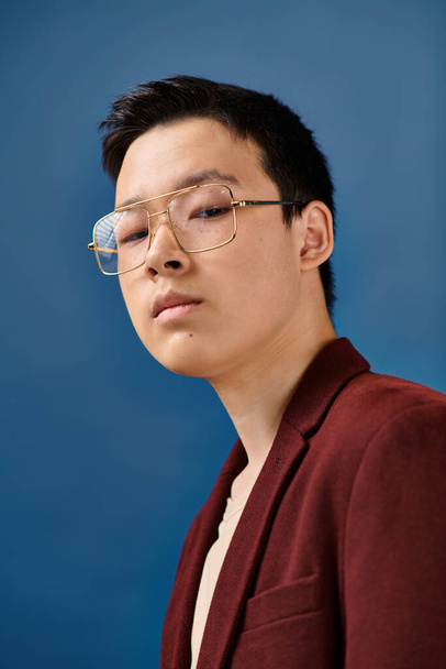 goed uitziende aziatische tiener jongen met bril in stijlvolle kleding op zoek naar camera op blauwe achtergrond - Foto, afbeelding