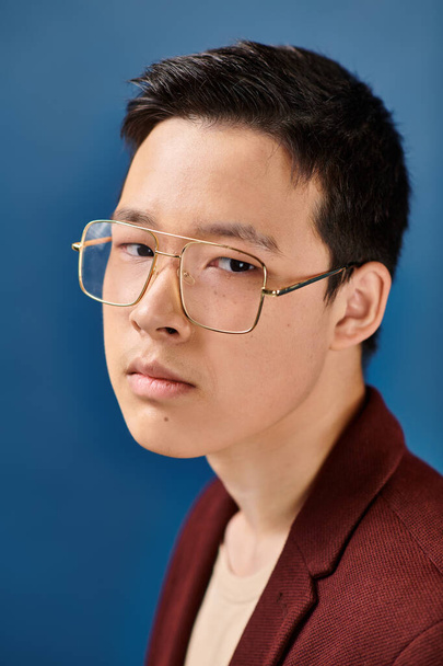 bonne recherche asiatique adolescent garçon avec lunettes dans élégant tenue en regardant caméra sur fond bleu - Photo, image