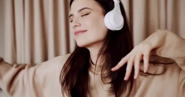 Mindful young happy woman wearing wireless headphones, listening relaxing music, resting on comfortable sofa, enjoying interesting audio book or affirmations, spending leisure indoors - Metraje, vídeo