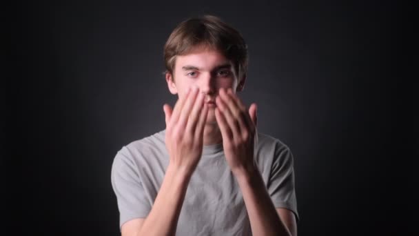 Serious Caucasian man, dressed casually, covers face with hands in a moment of introspection against a neutral black backdrop. His composed expressions and the gesture convey a sense of deep thought. - Footage, Video