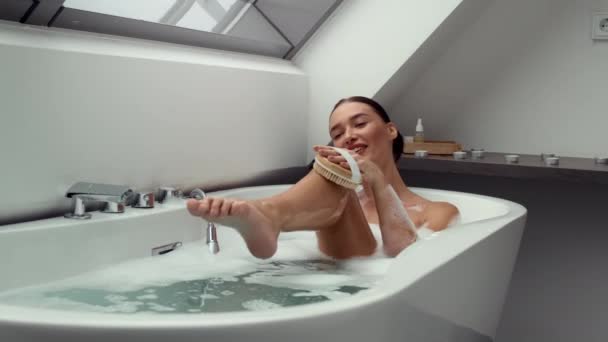 4K kuvamateriaalia, onnellinen nainen kupla-rikas kylpy, käyttäen kuorinta käsi hangata harjalla varovasti puhdistaa hänen jalkansa, hidastettuna. Puhdasta rentoutumista ja hemmottelua seesteisessä ilmapiirissä - Materiaali, video