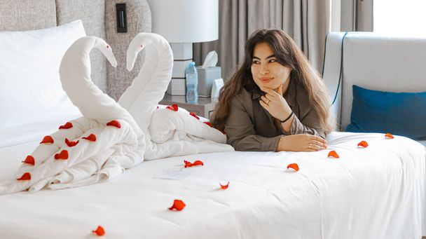 Portrait de la femme avec décoration de serviette de cygne sur lit avec oreiller blanc à l'intérieur de la chambre. Photo de haute qualité - Photo, image