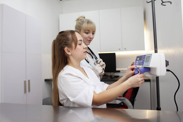 two female nurses in uniform use an infusator in a hospital, doctors connect the equipment against the background of the workplace - Foto, imagen