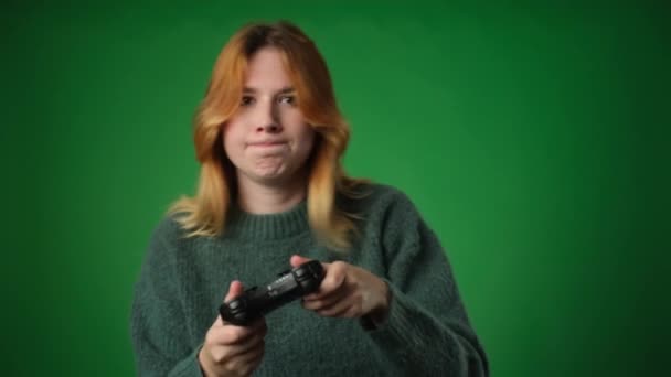 熱心な白人女性は,気軽に服を着て,ゲームパッドを使用し,緑色の背景に対してビデオゲームで敗北を経験します. 彼女の焦点を当てた表現とジェスチャーは,競争心を伝える. - 映像、動画