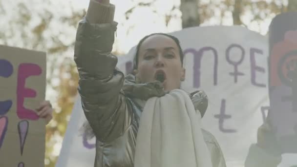 Сосредоточьтесь на эмоциональной молодой кавказке, стоящей на улице с поднятым кулаком и выкрикивающей феминистские лозунги с другими женщинами во время демонстрации протеста. - Кадры, видео