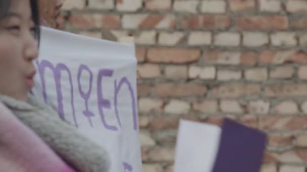 Команда многонациональных женщин-протестующих с демонстрационными плакатами и баннерами в руках марширует вместе вдоль улицы и выкрикивает лозунги суфражисток - Кадры, видео