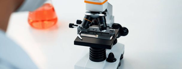 Εργαστηριακός ερευνητής αναπτύσσει νέα ιατρική ή θεραπεία χρησιμοποιώντας μικροσκόπιο. Τεχνολογική πρόοδος της υγειονομικής περίθαλψης με επιστημονική εμπειρογνωμοσύνη με εργαστηριακό εξοπλισμό μικροβιολογίας. Πανόραμα άκαμπτο - Φωτογραφία, εικόνα