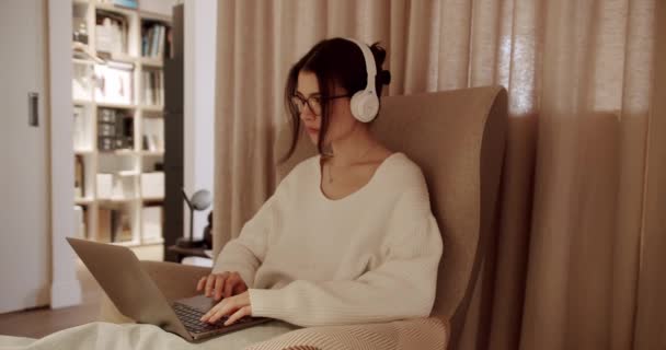 Kaunis nuori nainen työskentelee kannettavalla tietokoneella istuessaan tuolilla. Aistillinen tyttö yllään villapaita toimii Notebook. Tutkimukset, Surffaa Internetissä, Käyttää sosiaalista mediaa rentoutuen kodikas huoneisto - Materiaali, video