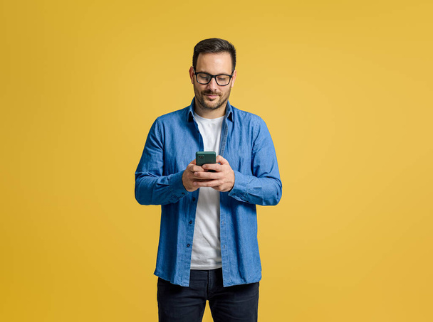 黄色の背景に隔離された携帯電話上のメッセージをチェックする自信のある深刻なビジネスマン - 写真・画像