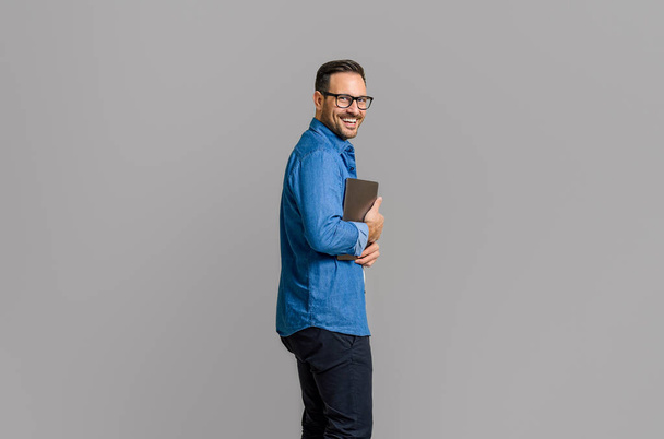 Vista laterale di un uomo d'affari sorridente che tiene il computer wireless mentre posa su uno sfondo bianco isolato - Foto, immagini