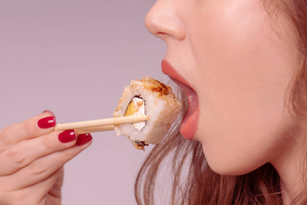 Young woman with red nails is eating sushi close up. - Foto, Imagen