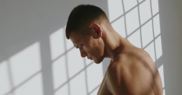 Πορτρέτο του νεαρού όμορφου bodybuilder με αθλητικό σώμα στο στούντιο με λευκό φόντο. Σοβαρό μυϊκό αρσενικό σε προπόνηση. Έννοια κινήτρου - Πλάνα, βίντεο