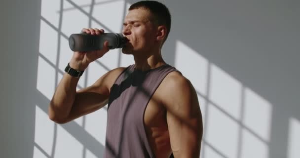 L'uomo atletico tiene in mano una bottiglia d'acqua e beve dopo l'allenamento. Giovane maschio si sentono assetati e ricostituire l'equilibrio idrico durante la pausa nell'esercizio. Stile di vita sano concetto - Filmati, video