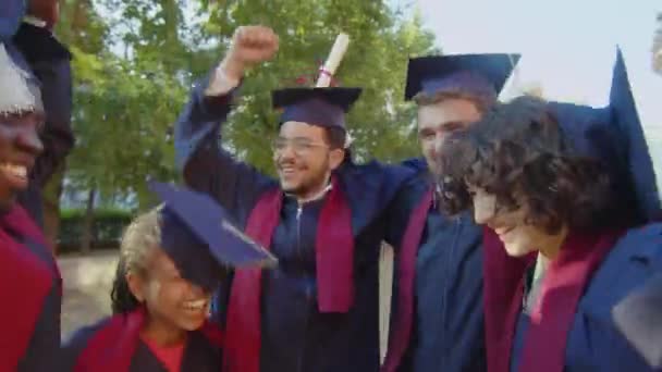 Inquadratura media di gruppi multietnici di studenti in abiti e cappelli molto eccitati che celebrano la loro laurea - Filmati, video
