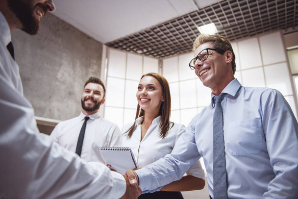 成功したビジネス人々 が青写真を議論しているし、事務所で作業しながら笑みを浮かべて、男性は握手を交わしています。 - 写真・画像