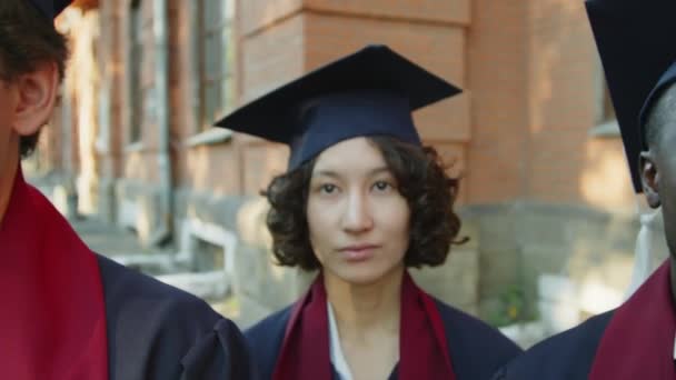 Primo piano di uomini e donne multietnici in cappelli e camici che ascoltano il rappresentante dell'università durante la cerimonia di laurea - Filmati, video