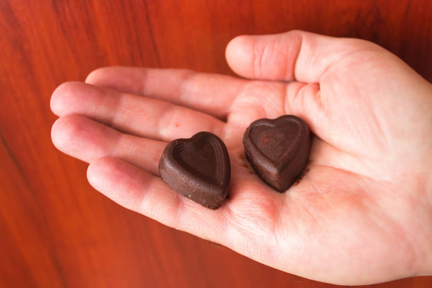 Doces de chocolate em forma de coração na mão em um fundo de madeira. - Foto, Imagem