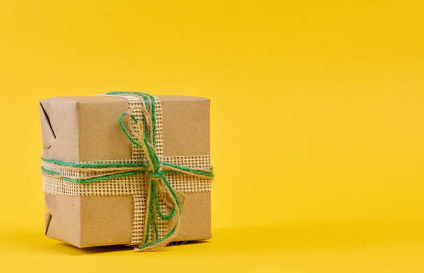 The box is packed in brown craft paper and tied with a rope on a beige background, gift - Photo, Image