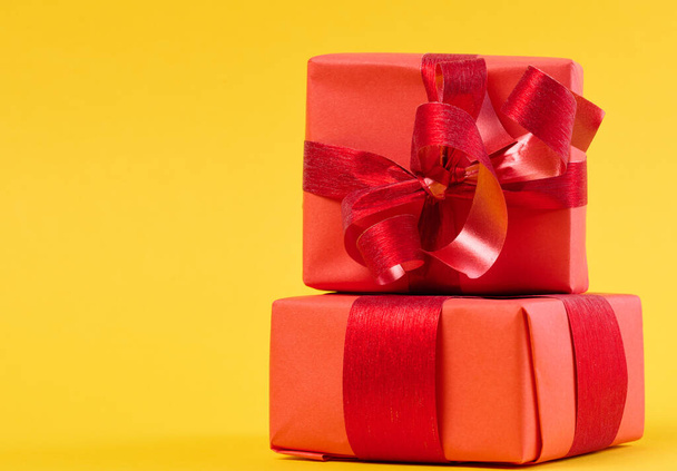 Doos is verpakt in rode geschenkverpakking en rood lint op een gele achtergrond - Foto, afbeelding