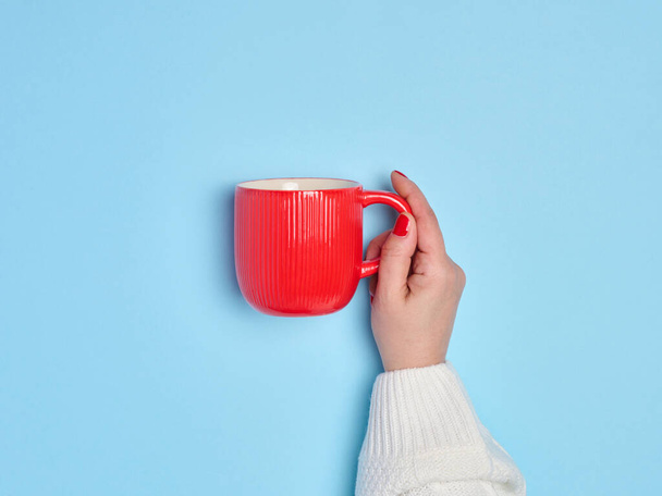 Female hand holding a red ceramic cup on a blue background - Photo, Image