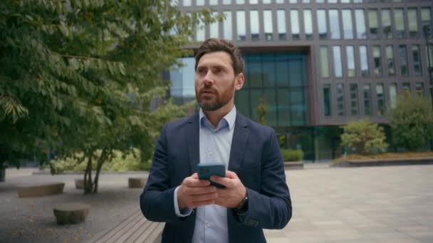 Kaukázusi mosolygós boldog felnőtt középkorú üzletember a városban séta okostelefonnal 40-es évek sikeres üzletember kommunikáció online mobiltelefon séta férfi szakmai technológia szabadtéri - Felvétel, videó