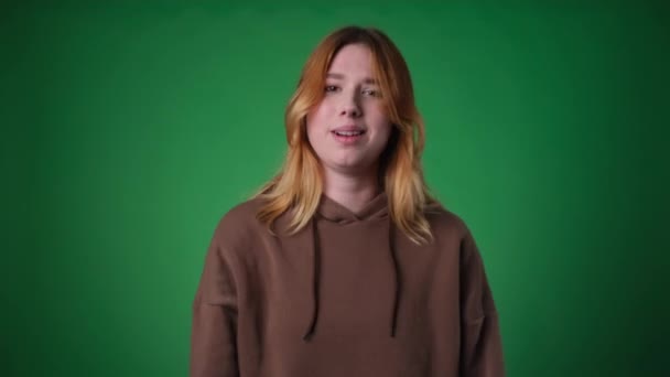 Charismatic Caucasian woman, dressed casually, engages in a conversation on a green backdrop. Her expressive communication style and dynamic presence capture the essence of modern content creation. - Footage, Video