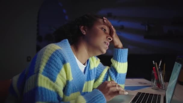 Jeune étudiante américaine noire ennuyée et fatiguée, écrivant et utilisant un ordinateur portable assis au bureau à la maison dans la chambre, étudiant à distance, travaillant en ligne la nuit. Vue latérale génération Z femme à la recherche pc. - Séquence, vidéo
