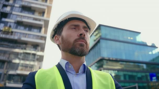 Kaukázusi középkorú férfi felnőtt férfi vállalkozó visel sisak és reflektív mellény építész töprengő gondolkodás a városban körülnézett városi épület építész építész üzleti építész mérnök - Felvétel, videó