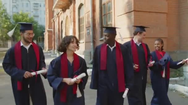 Tracciamento medio lungo di diversi team di studenti laureati in abiti e cappelli che comunicano tra loro - Filmati, video